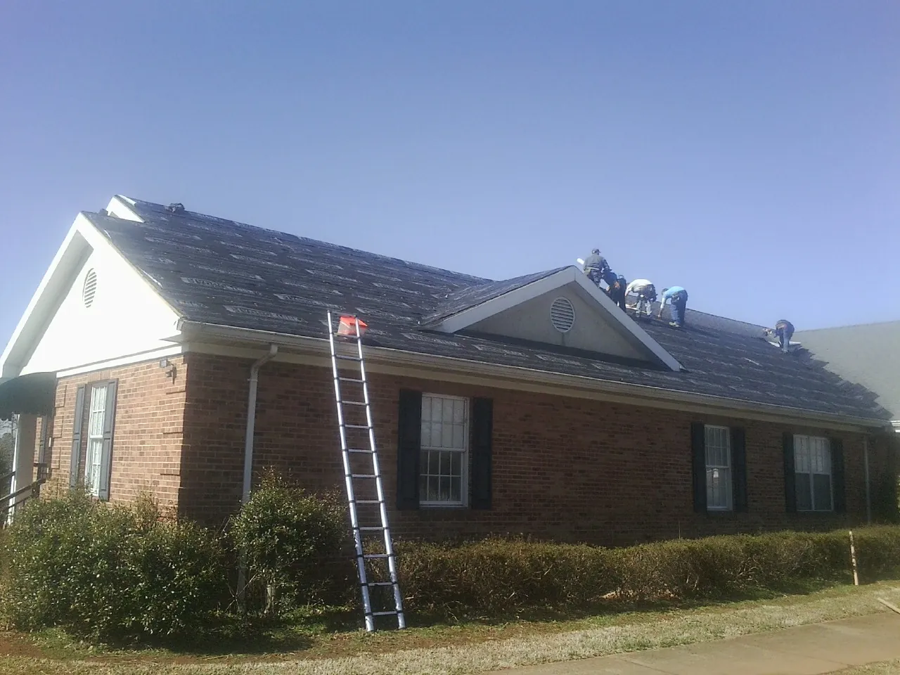 Crew tearing shingles off a brick ranch roof with a ladder set — Emergency Roof Repair work by our crew in Bailey Island