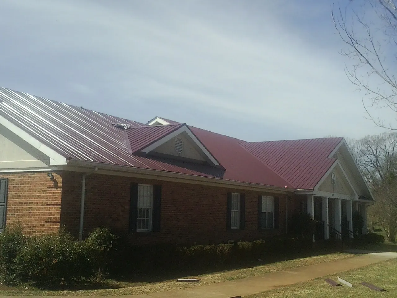 Red metal roof with gabled entries on a long brick building, from a Hail Damage Roof Repair job in Bailey Island