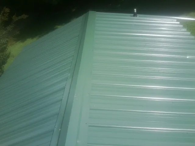 New green metal panels meeting at the ridge of a roof — Flat Roof Repair work by our crew in Bailey Island