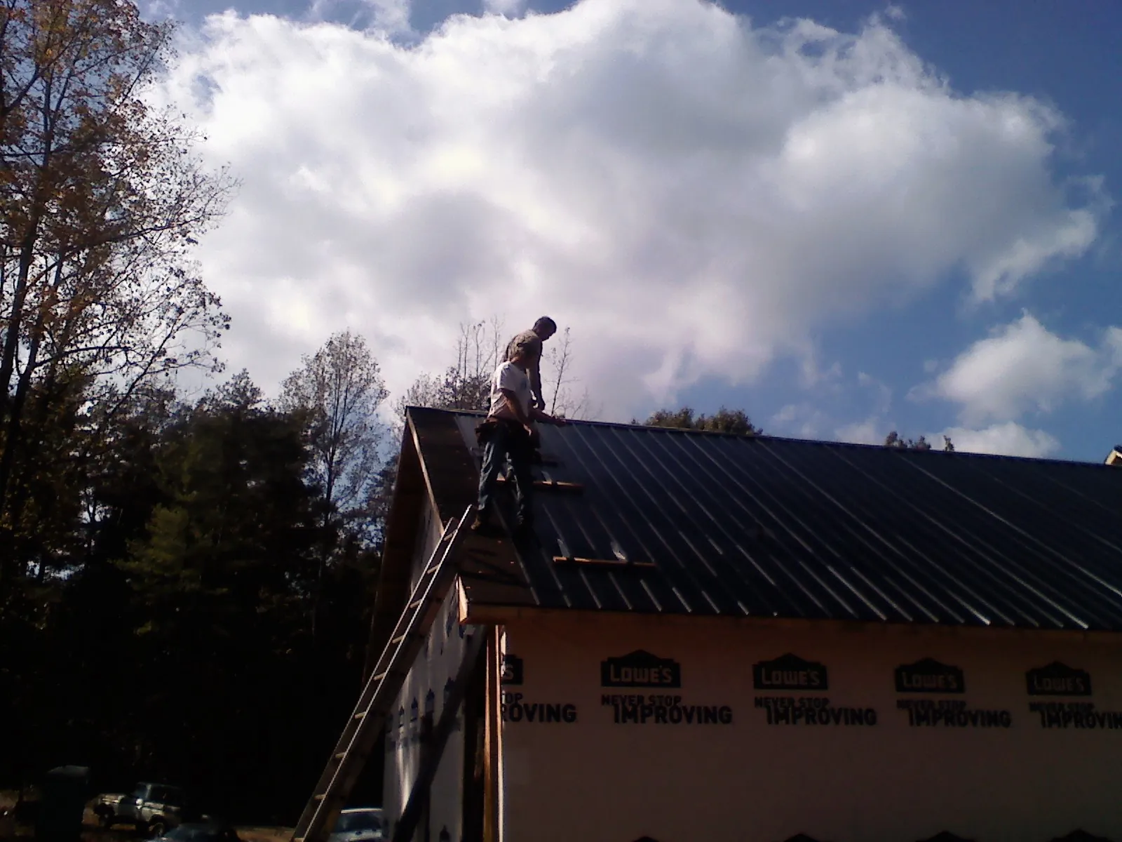 Roofer fastening dark metal panels high against a cloudy sky, from a Roof Inspection job in Bailey Island