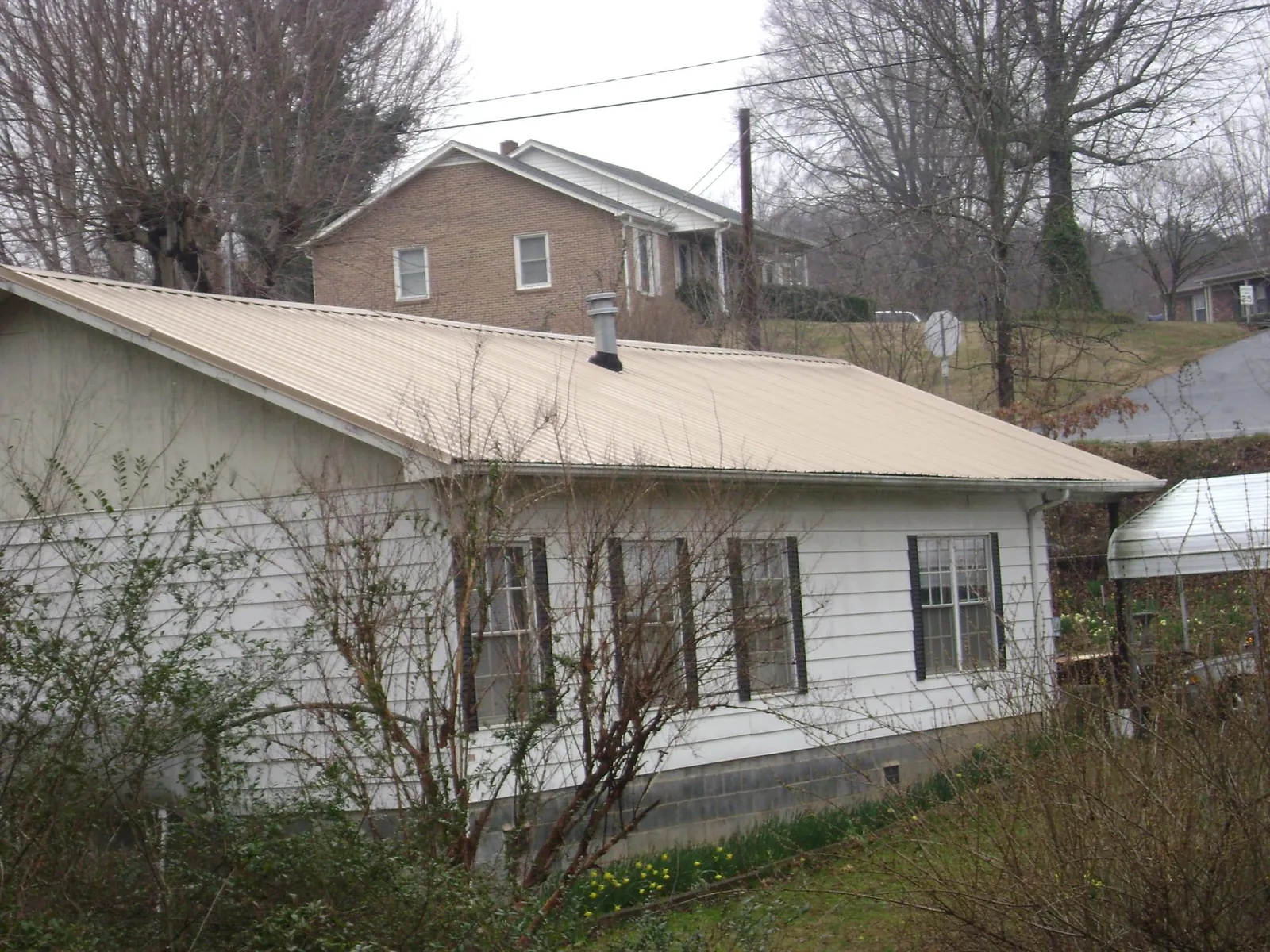 Tan metal roof on a white sided house set into a hillside — Commercial Roofing by Roofing Brothers in Bailey Island